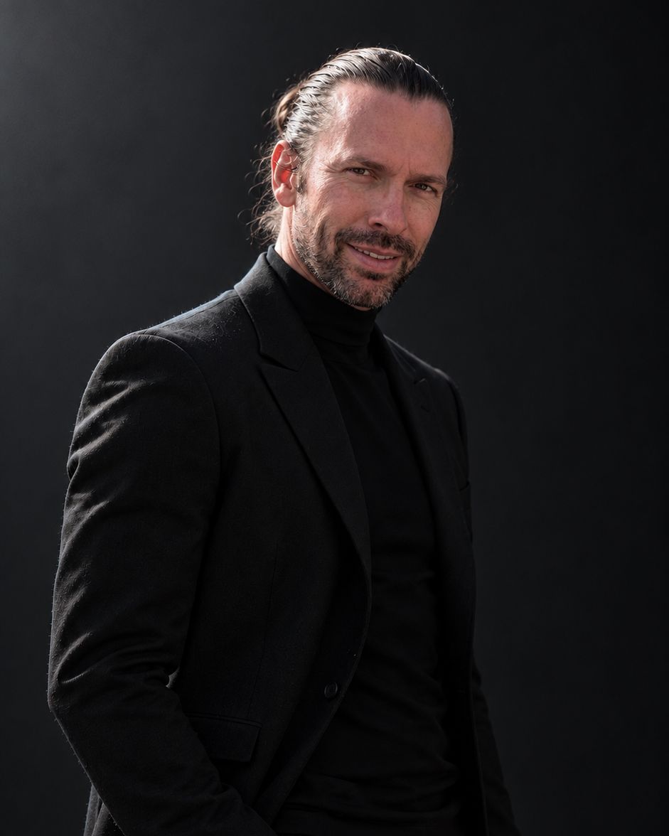 Stephan smiling at the camera, in a black suit and turtleneck.