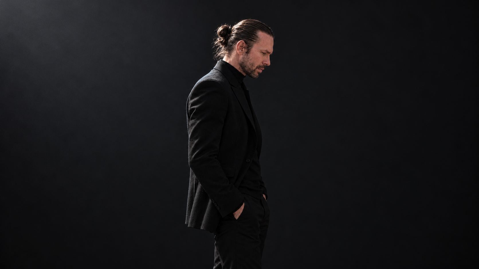 Stephan in side profile, in a black suit against a charcoal background.